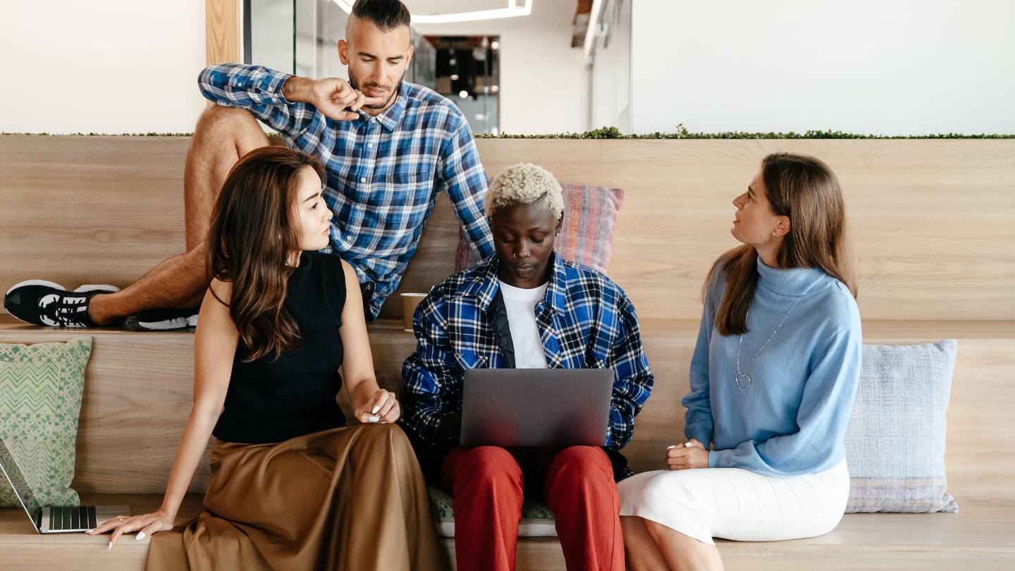 Four junior employees sit around a laptop, having a meeting in an office.